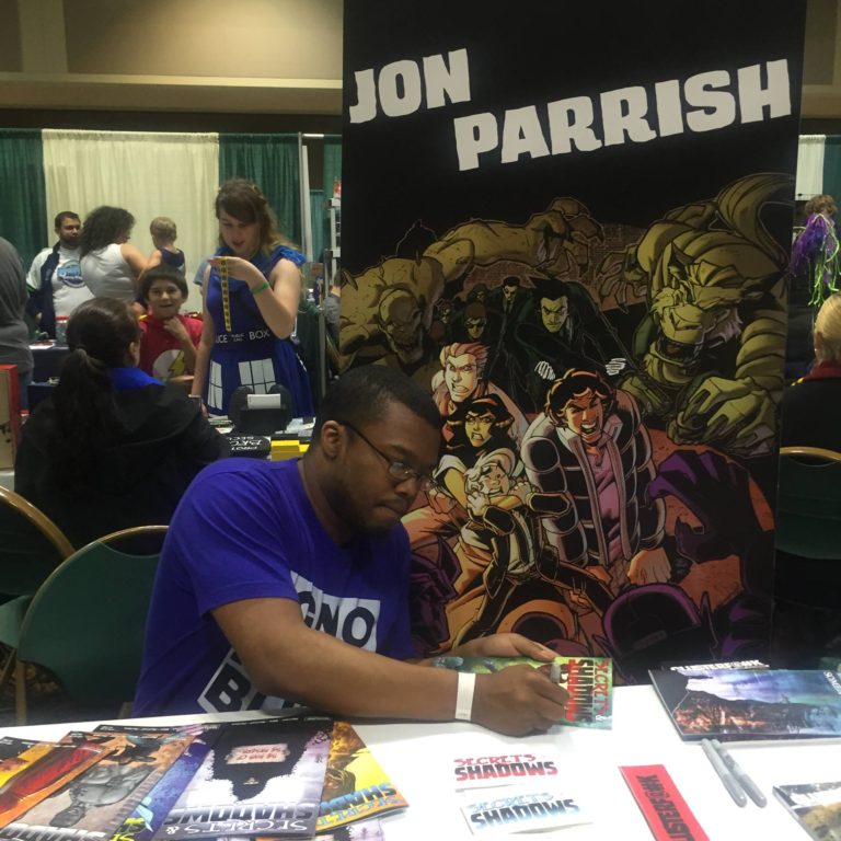 Jon Parrish, writer and creator of SECRETS AND SHADOWS and CLUSTERF#%K, mans his table at St. Louis Comicon (picture from shadowsandsecrets.net)